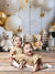 Twin toddlers crawling on a rustic wood floor with gold and white balloons, teddy bears, and presents in the Bears and Stars Cake Smash Backdrop setup.