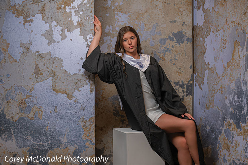 Caspian Silver and Beige Weathered Texture, photography backdrop panel for Denny StudioEdge silicone edge frame, shown with a senior girl in a graduation gown seated on a white posing cube with an arm raised on the wall SECP-8856