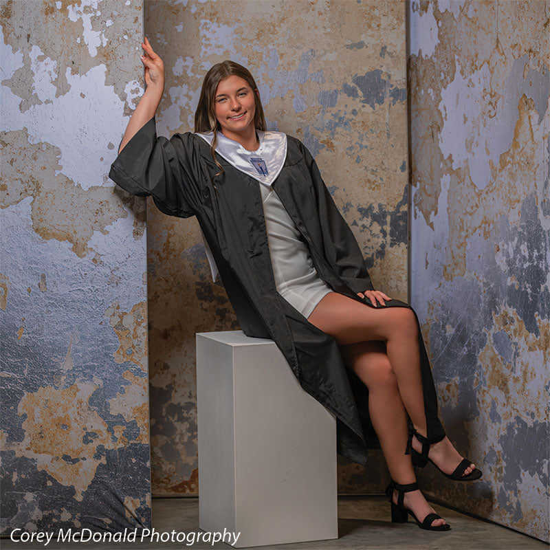 Caspian Silver and Beige Weathered Texture, photography backdrop panel for Denny StudioEdge silicone edge frame, shown with a senior girl in a graduation gown seated on a white posing cube, legs crossed SECP-8856