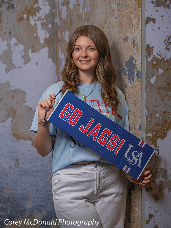 Caspian Silver and Beige Weathered Texture, photography backdrop panel for Denny StudioEdge silicone edge frame, shown with a senior girl leaning on the wall holding a rolled Go Jags banner SECP-8856