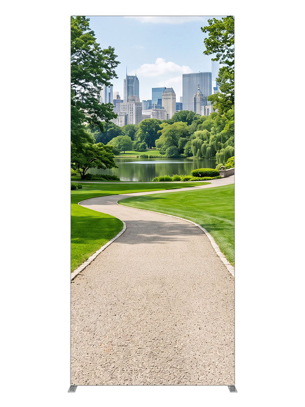A landscaped city park with a winding gravel path, lake and flower borders below a distant skyline, 3ft photography backdrop panel for Denny StudioEdge silicone edge frame