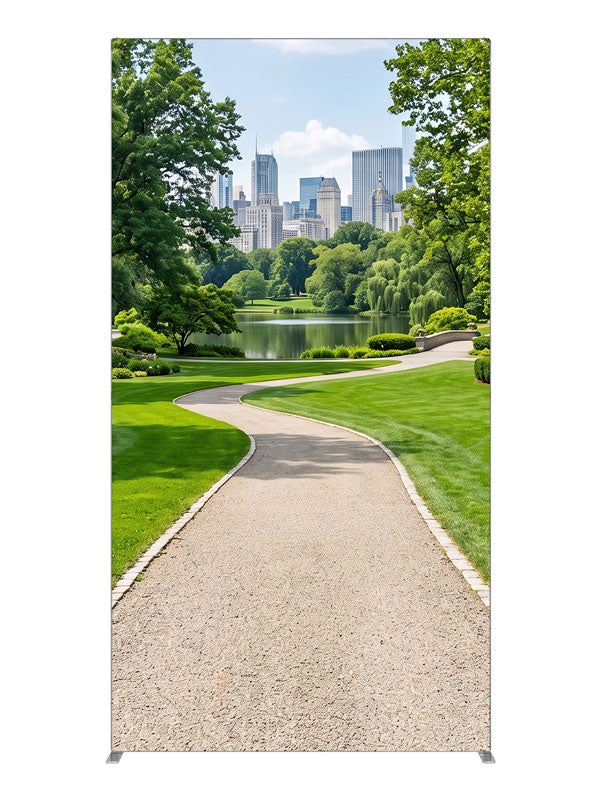 A landscaped city park with a winding gravel path, lake and flower borders below a distant skyline, 4ft photography backdrop panel for Denny StudioEdge silicone edge frame