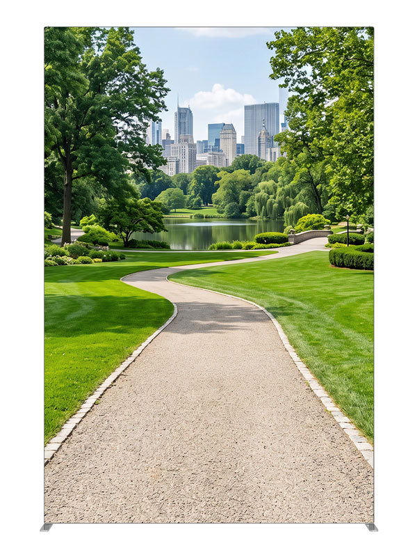 A landscaped city park with a winding gravel path, lake and flower borders below a distant skyline, 5ft photography backdrop panel for Denny StudioEdge silicone edge frame