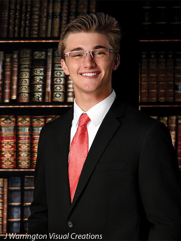 Teen boy in formal attire smiling in front of a classic library bookshelf backdrop, perfect for graduation portraits or academic-themed photo sessions.