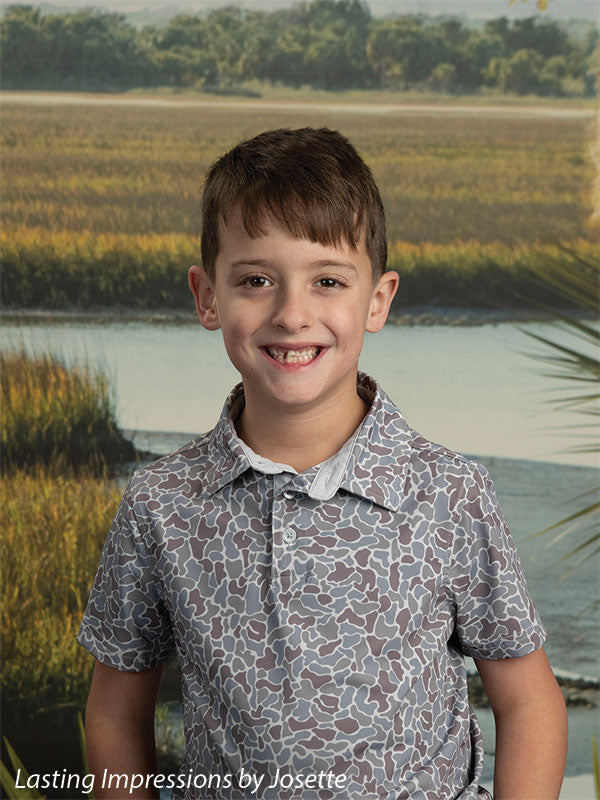 Coastal Marsh View photography backdrop showing golden marsh grass and a tidal creek with a distant treeline and palmetto fronds, shown with a young boy in a patterned short-sleeve shirt in a close half-length portrait CP-8486