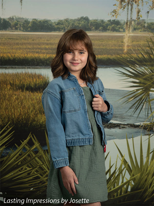 Coastal Marsh View photography backdrop showing golden marsh grass and a tidal creek with a distant treeline and palmetto fronds, shown with a young girl in a denim jacket over an olive skirt CP-8486