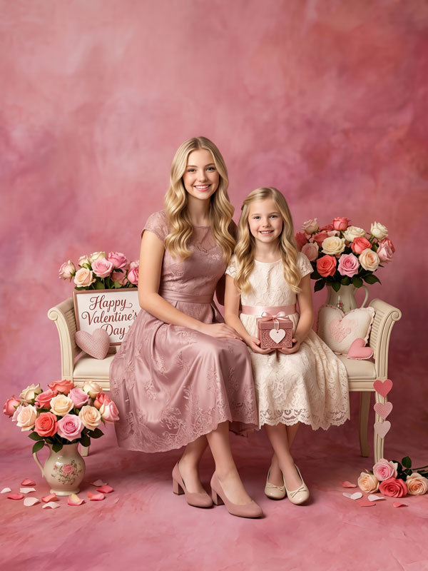 Coral Haze coral pink mottled texture photography backdrop, shown with a woman and a young girl in pink dresses seated among roses in a Valentine's Day setup CP-9014