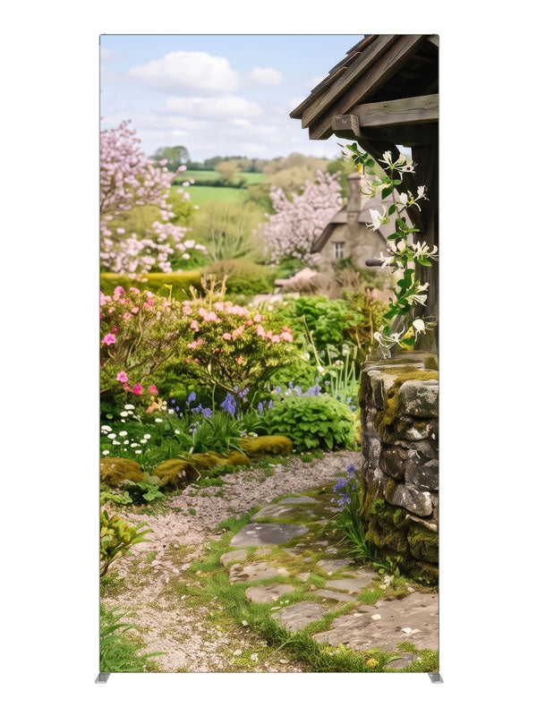 A spring cottage garden with a stone wishing well, a flowering path and a cottage with green hills, 4ft photography backdrop panel for Denny StudioEdge silicone edge frame