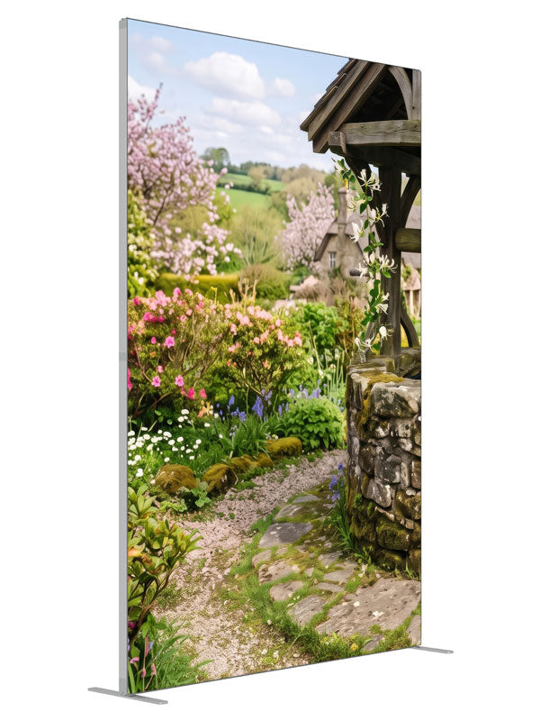A spring cottage garden with a stone wishing well, a flowering path and a cottage with green hills, 5ft photography backdrop panel for Denny StudioEdge silicone edge frame, angled view