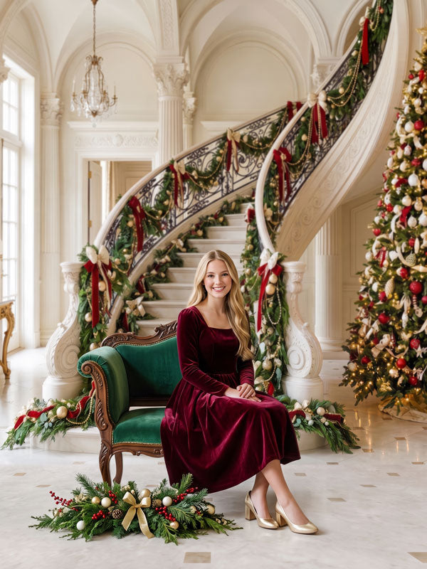 Crystal Noel palatial white foyer with curved staircase and chandelier photography backdrop shown with a woman in a burgundy velvet dress seated on a green settee CP-8908