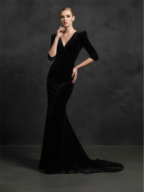 A woman wearing a long black gown poses elegantly against a dark charcoal studio backdrop with a moody textured finish and dramatic tonal depth.
