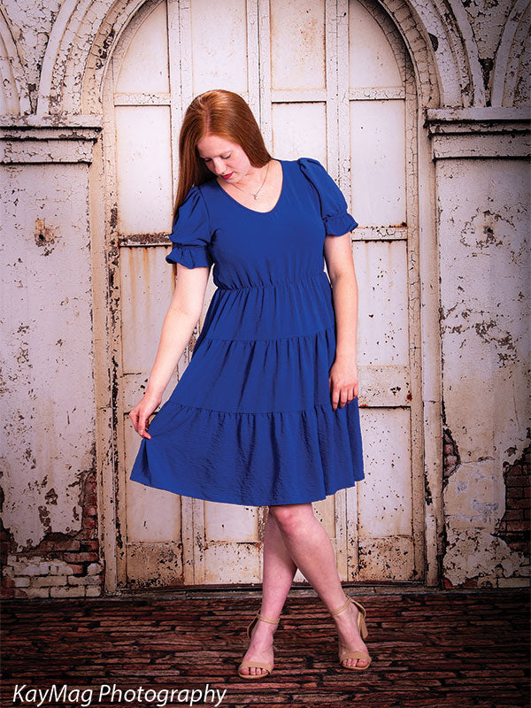 Teen girl looking down while holding her dress in front of a rustic white arched door and vintage brick floordrop, perfect for styled senior portraits.