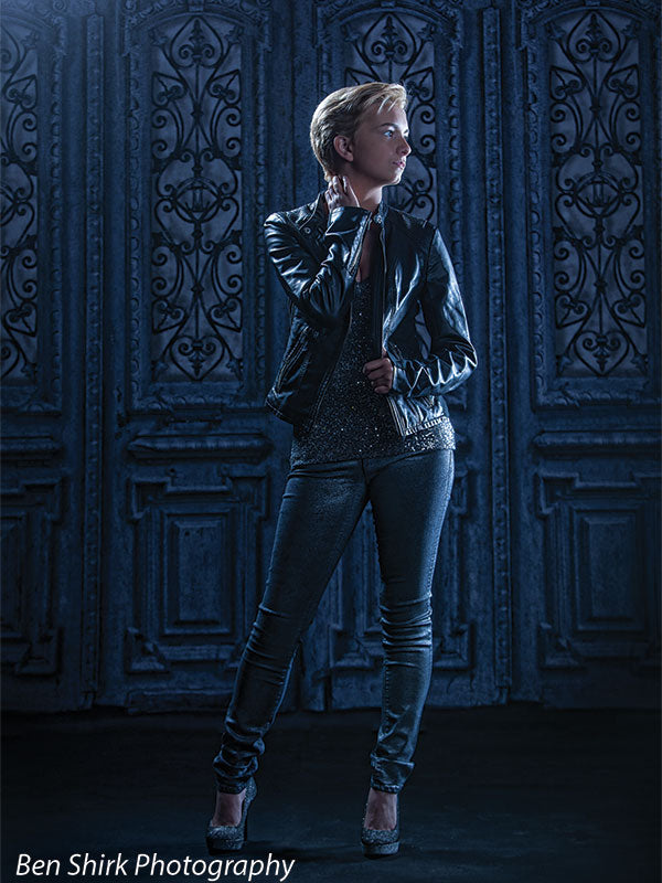 Teen model in shimmering attire stands confidently in front of a vintage blue door backdrop with iron paneling, ideal for high-contrast editorial photo sessions.