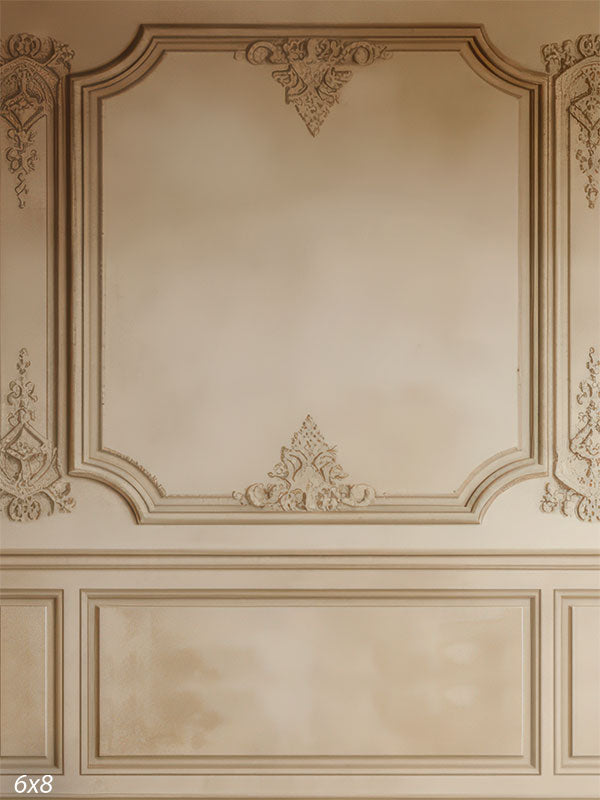 A beige paneled wall with ornate moldings, scrollwork, and soft patina, evoking timeless European elegance.