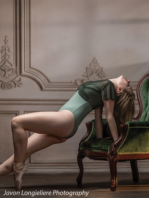 Elegant French Panel Wall photography backdrop with an antique green velvet armchair, shown with a young ballet dancer arching back against the chair en pointe in a wider view CP-8744