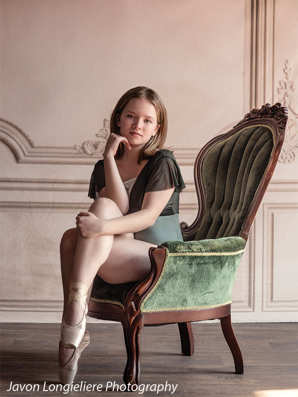 Elegant French Panel Wall photography backdrop with an antique green velvet armchair, shown with a young ballet dancer perched on the chair arm with a knee up and hand to her chin CP-8744