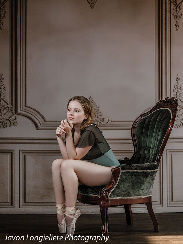 Elegant French Panel Wall photography backdrop with an antique green velvet armchair, shown with a young ballet dancer seated on the chair with hands clasped in a contemplative pose CP-8744