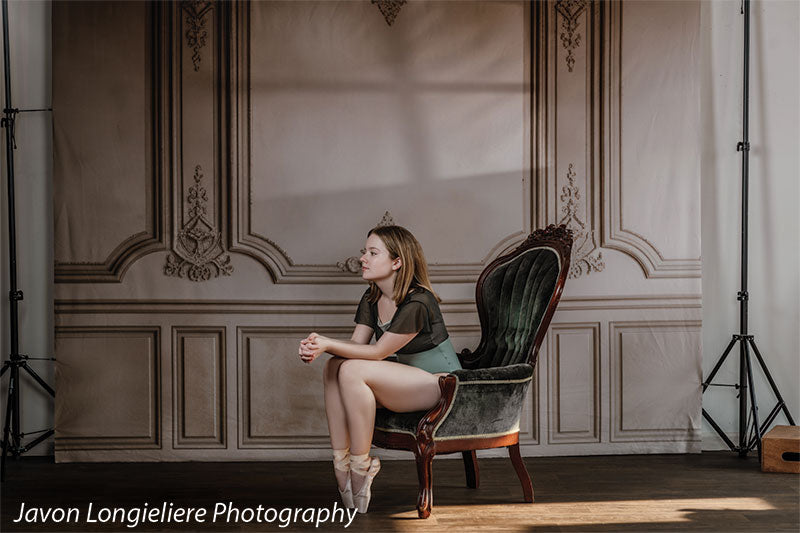 Elegant French Panel Wall photography backdrop with an antique green velvet armchair, shown with a young ballet dancer in an olive leotard and pointe shoes seated on the chair with hands clasped CP-8744