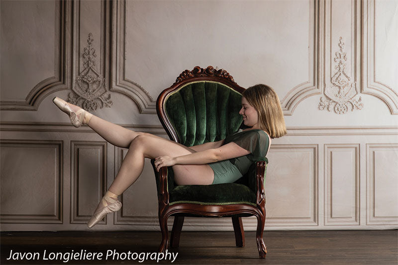 Elegant French Panel Wall photography backdrop with an antique green velvet armchair, shown with a young ballet dancer seated sideways with her legs over the chair arm CP-8744