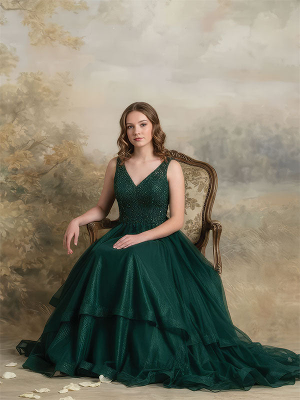 A woman in a dark green formal gown sits on an upholstered chair, posed against an elegant painted landscape backdrop with soft neutral tones and a refined painterly texture.
