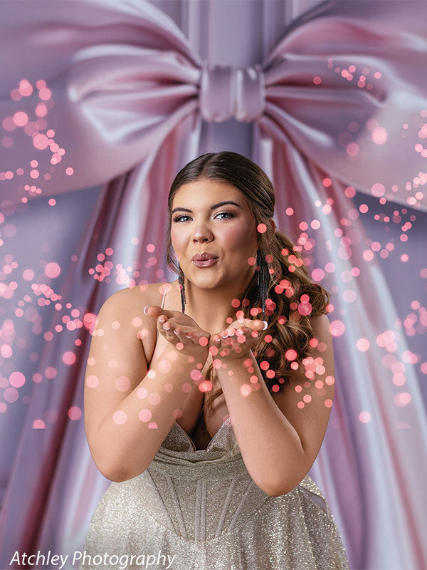 Pink satin bow studio backdrop with a model in a sparkling gold dress blowing pink confetti, perfect for glam or celebration portrait photography.