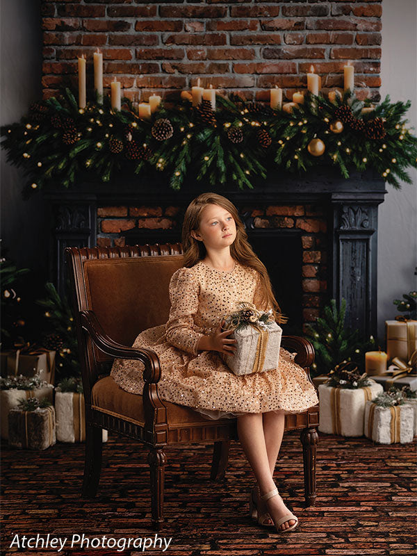 Ember & Pine brick fireplace with Christmas garland photography backdrop shown with a girl in a gold sequin dress seated on a chair holding a wrapped gift CP-8881
