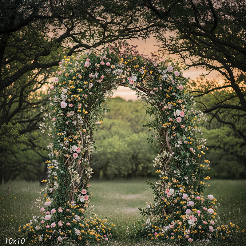 Spring forest floral arch framed by dark tree branches and warm evening sky, standing in a grassy meadow filled with small wildflowers.