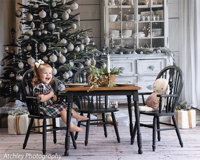 Horizontal farmhouse Christmas backdrop with decorated tree, white hutch, rustic dining table, and holiday gifts, featuring a young girl and plush toy, great for festive children’s photography.