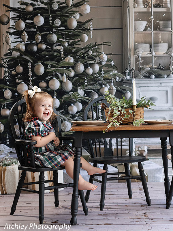 Close-up of farmhouse Christmas backdrop with decorated tree and vintage hutch, shown with a young girl laughing in a plaid dress, perfect for intimate seasonal portraits.