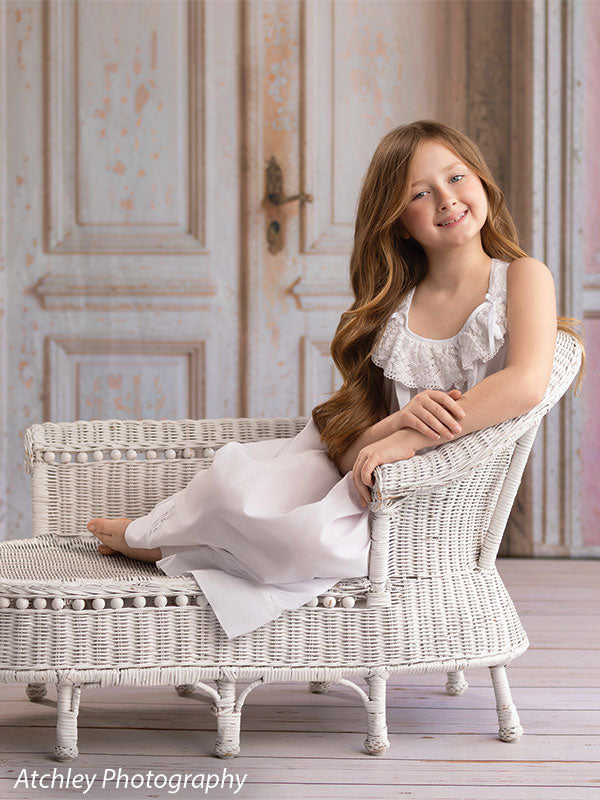 Farmhouse whitewash wood photography floor drop shown with a young girl on a white wicker settee atop the whitewash wood floor FD-4270