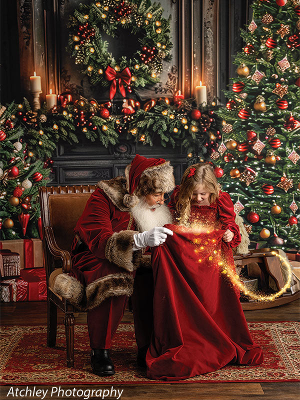 Santa Claus leaning toward a young girl in a red dress as she looks down at sparkling lights in her skirt, seated in front of a festive Christmas fireplace backdrop with a decorated tree, wreath, glowing garland, candles, and wrapped gifts.