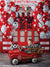 Young boy riding a red firetruck pedal car in front of a festive firehouse cake smash backdrop with red and white balloons and firefighter dalmatian plush toys.