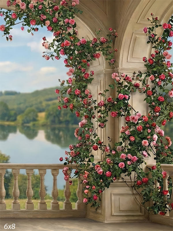 This photography backdrop shows a stone arch terrace with rose vines, a balustrade, and a countryside landscape beyond. The studio background provides architectural depth and floral detail behind a portrait subject.