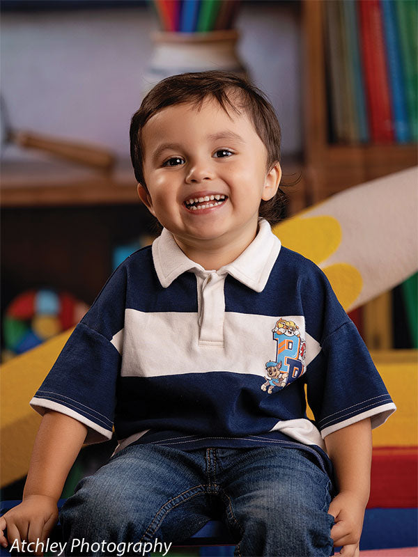 Giant yellow pencil photography prop softly out of focus behind a smiling toddler boy in a close-up classroom-themed portrait GCP