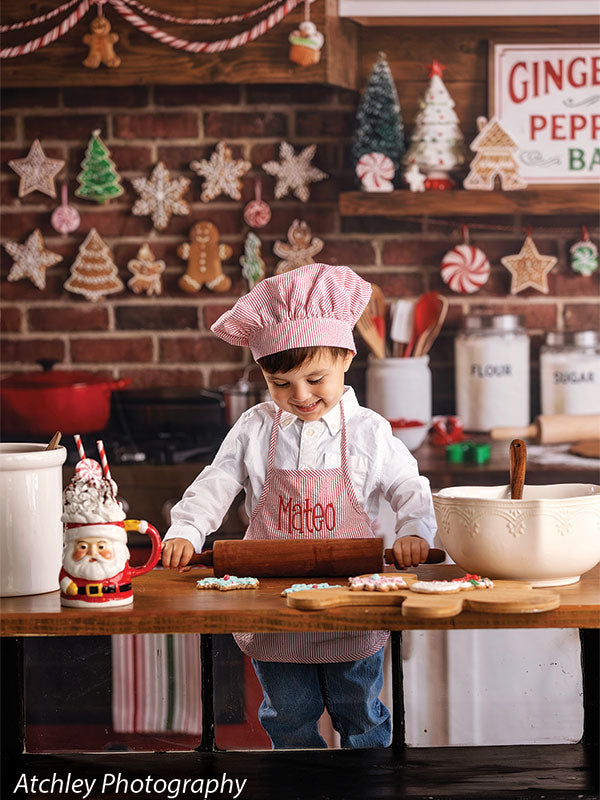 Ginger Street gingerbread bakery kitchen photography backdrop shown with a young boy in a pink chef hat and apron rolling dough at the counter CP-8876