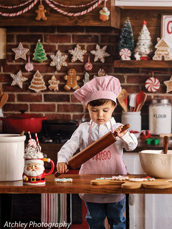 Ginger Street gingerbread bakery kitchen photography backdrop shown with a young boy in a pink chef hat and apron rolling out cookie dough CP-8876