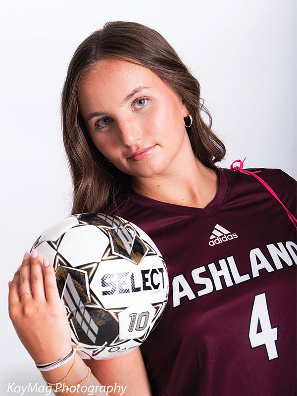 Confident soccer player in Ashland jersey posing with a Select soccer ball on a bright white vinyl photography backdrop.