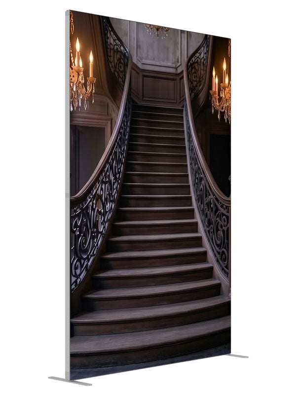 An opulent mansion foyer staircase with iron scroll railings and lit crystal chandeliers, 5ft photography backdrop panel for Denny StudioEdge silicone edge frame, angled view
