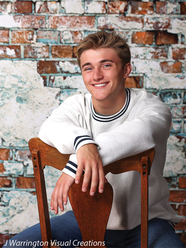 High school senior posing casually against a grunge-style brick and plaster backdrop, styled for professional studio portrait settings.