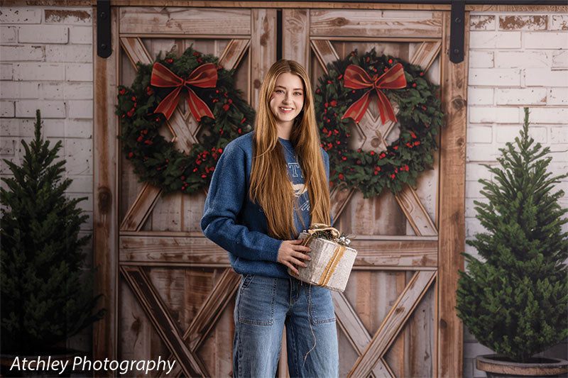 Holly Barn rustic barn doors with Christmas wreaths photography backdrop shown with a senior girl holding a wrapped gift by the barn doors, wide view CP-8918