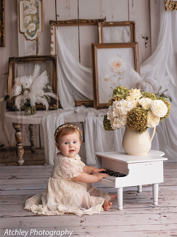 Baby playing piano on the rustic Ivory Antique Wood Plank floor drop, with vintage picture frames and soft fabric backdrop.