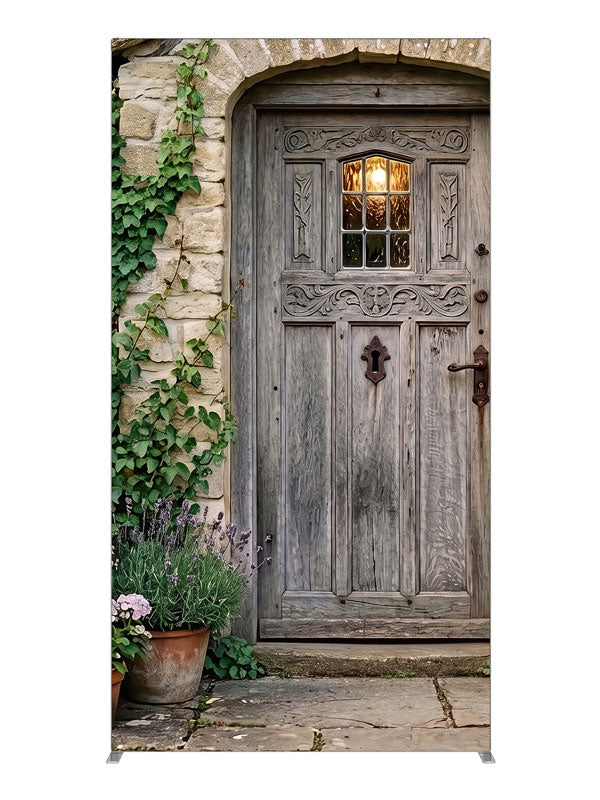Arched weathered plank cottage door in a honey stone wall with climbing ivy, lavender and potted hydrangeas, 4ft photography backdrop panel for Denny StudioEdge silicone edge frame