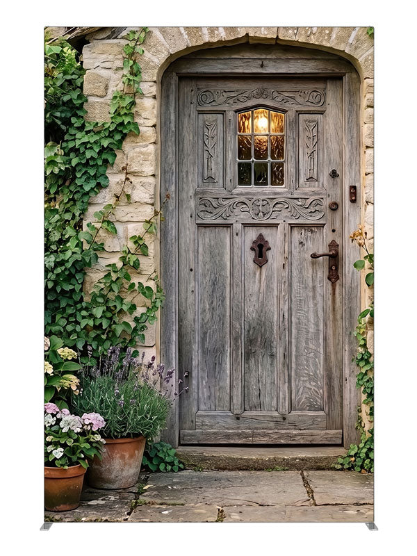 Arched weathered plank cottage door in a honey stone wall with climbing ivy, lavender and potted hydrangeas, 5ft photography backdrop panel for Denny StudioEdge silicone edge frame