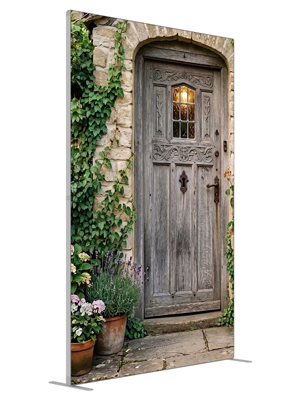 Arched weathered plank cottage door in a honey stone wall with climbing ivy, lavender and potted hydrangeas, 5ft photography backdrop panel for Denny StudioEdge silicone edge frame, angled view