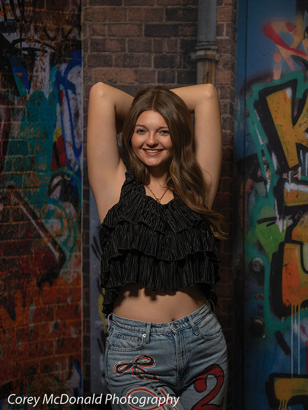 Keaton Graffiti Warehouse Door, photography backdrop panel for Denny StudioEdge silicone edge frame, shown with a senior girl in a black ruffle top smiling with arms overhead SECP-8864