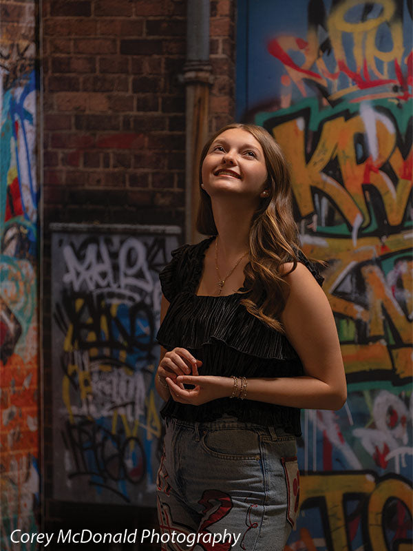 Keaton Graffiti Warehouse Door, photography backdrop panel for Denny StudioEdge silicone edge frame, shown with a senior girl in a black ruffle top smiling upward with hands clasped SECP-8864