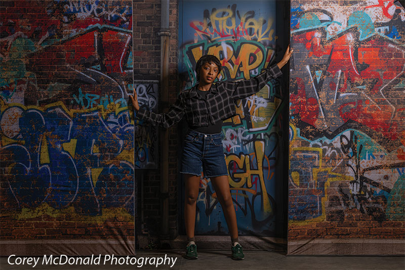 Keaton Graffiti Warehouse Door, photography backdrop panel for Denny StudioEdge silicone edge frame, shown with a senior girl leaning with one arm raised on the graffiti wall SECP-8864