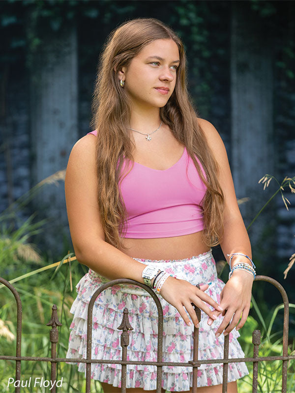 Lorian photography backdrop showing an ivy-covered classical garden wall with tall grasses and a wrought-iron fence, shown with a senior girl in a pink tank top and floral skirt with hands clasped CP-8852