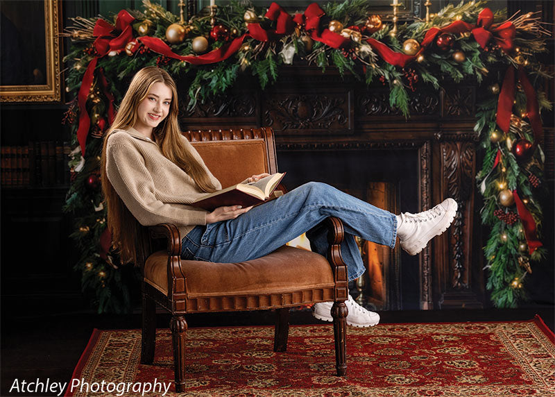 Manor Hearth dark wood fireplace with Christmas wreath photography backdrop shown with a senior girl reclining with a book on a leather chair in a wide view CP-8885