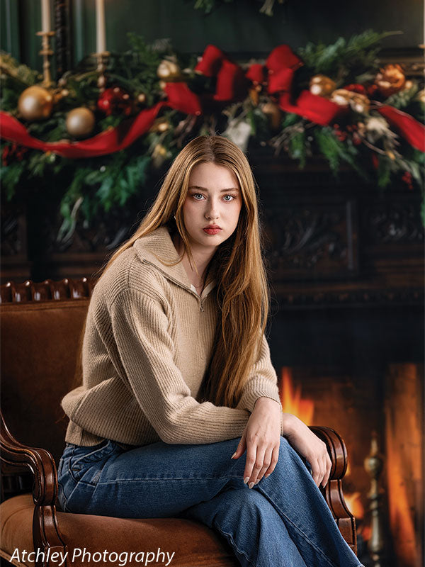 Manor Hearth dark wood fireplace with Christmas wreath photography backdrop shown with a senior girl in a tan sweater seated with her hand on her chin CP-8885